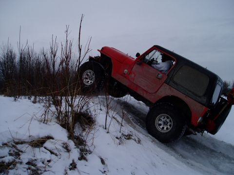 2000 Ford E350 - A red Jeep Wrangler navigates a slippery, snow-covered hill with its front-right wheel off the ground.