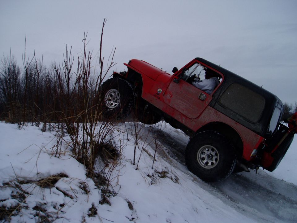 Red Jeep Wrangler with black top driving on a snowy incline, front-right wheel lifted