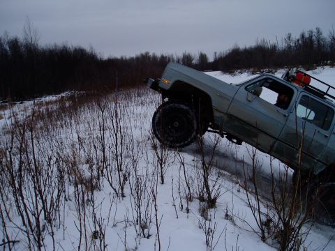 2000 Ford E350 - A light blue pickup truck with oversized tires navigates a snow-covered incline, its off-road capabilities.