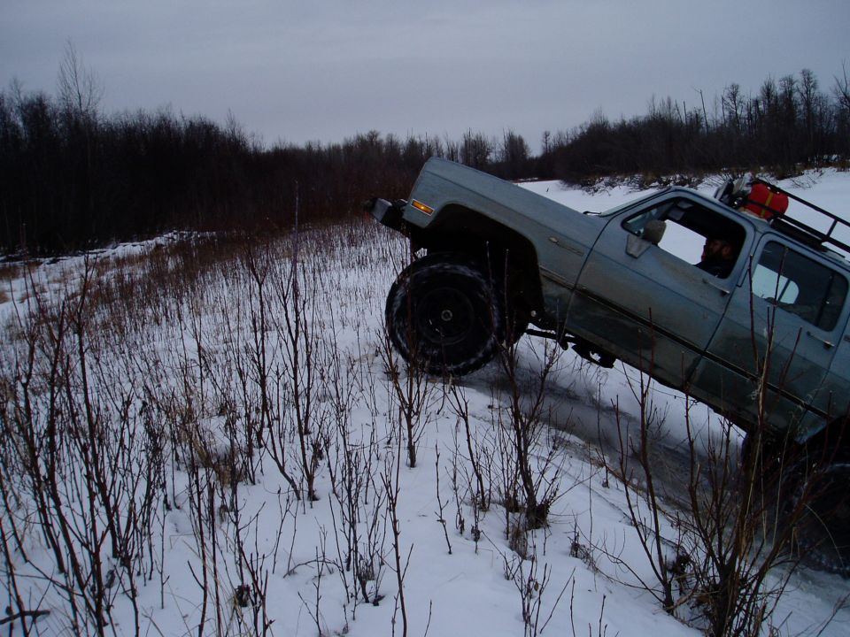 Light blue pickup truck with large tires driving on a snowy hill. The truck appears to be from the 1980s