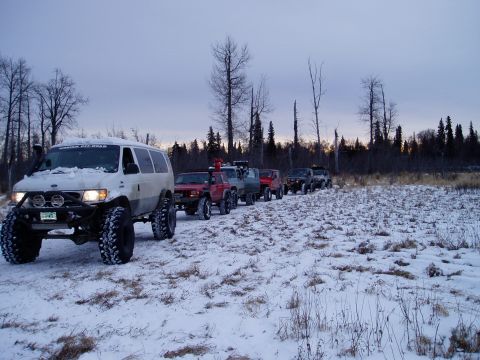 2000 Ford E350 - Several modified off-road vehicles, including a Ford E350 van, travel in a convoy across a snow-covered landscape.