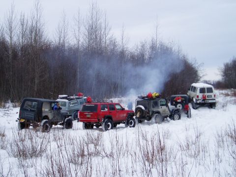 2000 Ford E350 - A group of off-road vehicles are gathered in a snowy landscape with smoke billowing from one of them.