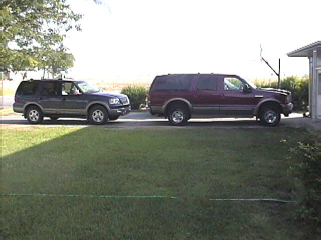Green Ford Expedition parked facing a dark red SUV with tan trim on a driveway next to grass