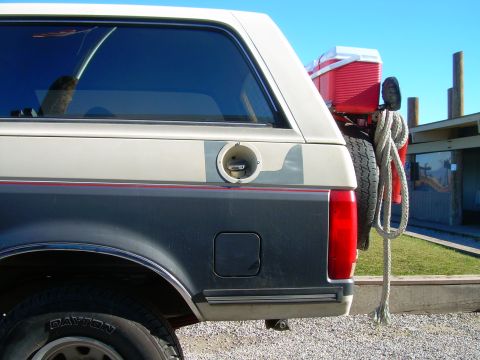 1991 Ford Bronco - This 1991 Ford Bronco shows its rear quarter panel, a spare tire mounted on the back and a red cooler.