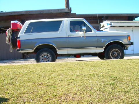 1991 Ford Bronco - Side profile of a 1991 Ford Bronco, showing its two-tone paint scheme and rear-mounted spare tire with a cooler.