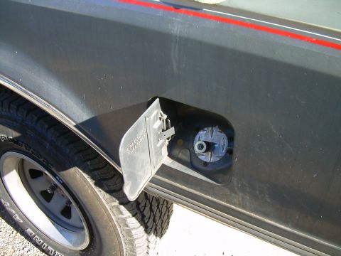 1991 Ford Bronco - The fuel door is open, revealing the gas cap receptacle and a portion of the vehicle's tire.