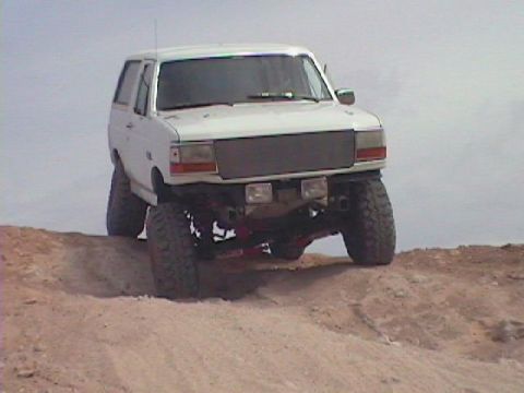 1992 Ford Bronco - White 1992 Ford Bronco with lifted suspension driving on a dirt incline.