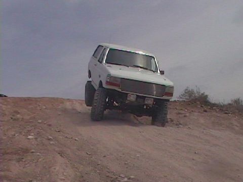 1992 Ford Bronco - This lifted 1992 Ford Bronco navigates a dusty, off-road incline under a hazy sky.