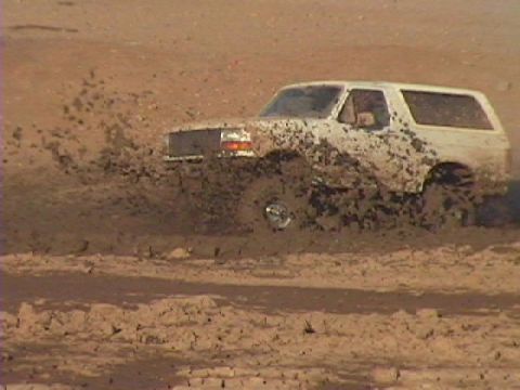 1992 Ford Bronco - White 1992 Ford Bronco driving through a muddy area, kicking up a lot of dirt.