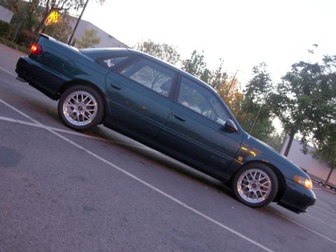 1995 Ford Taurus - A dark green 1995 Ford Taurus SHO is parked in an outdoor lot with trees in the background.
