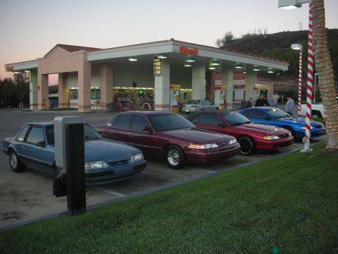 1992 Ford Crown Victoria - Four cars are lined up at a Shell gas station during twilight.