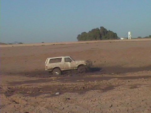 1992 Ford Bronco - A white SUV is stuck in a muddy area under a clear sky with dry terrain in the background.