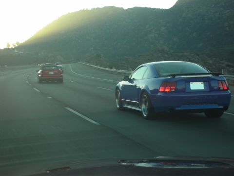 1992 Ford Crown Victoria - A blue Ford Mustang cruises down the highway with a red car ahead.