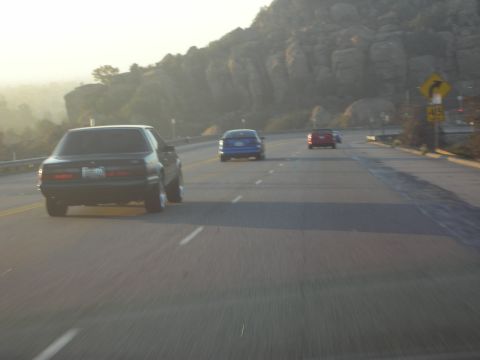 1992 Ford Crown Victoria - A dark 1987 Ford Mustang travels down a highway with other vehicles in the distance.