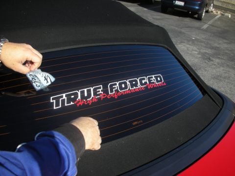 1992 Ford Crown Victoria - A person applies a 'True Forged High Performance Wheels' sticker to the rear window of a red convertible, with another car visible in the b…