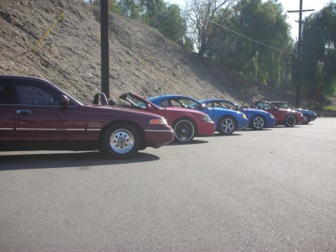 1992 Ford Crown Victoria - A line of cars, including a maroon 1992 Ford Crown Victoria, parked on asphalt.