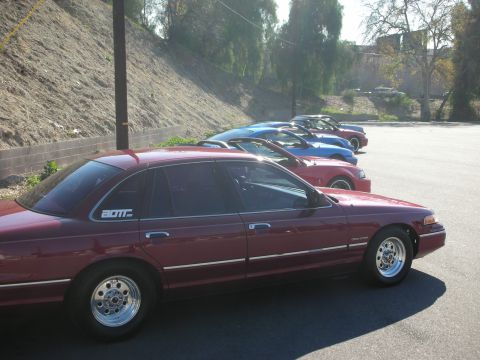1992 Ford Crown Victoria - A line of cars, including a maroon 1992 Ford Crown Victoria, are parked on a sunny day.