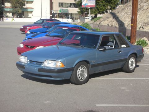 1992 Ford Crown Victoria - A line of cars are parked in a lot, with a blue coupe in the foreground.