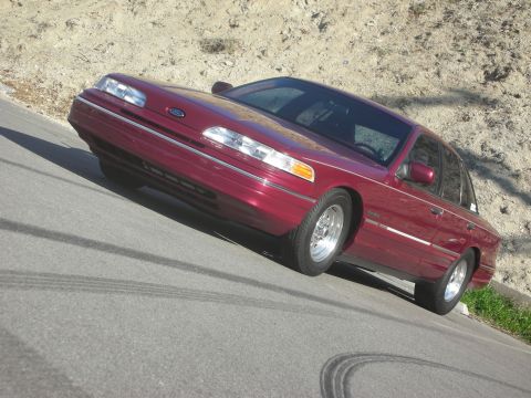 1992 Ford Crown Victoria - A red 1992 Ford Crown Victoria is parked on a road with tire marks visible on the asphalt.
