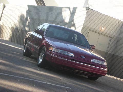 1992 Ford Crown Victoria - A maroon 1992 Ford Crown Victoria is parked in front of a building with a garage door.