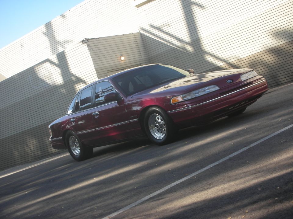 Maroon 1992 Ford Crown Victoria with aftermarket wheels parked near a brick building