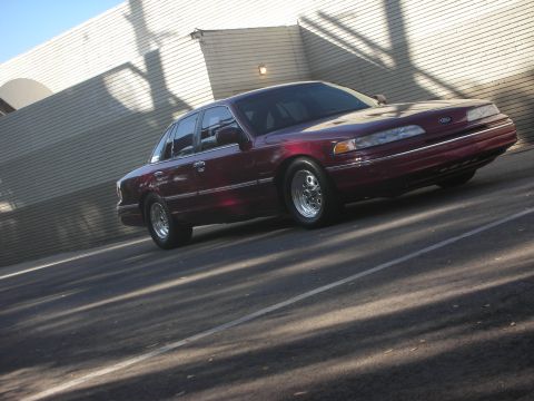 1992 Ford Crown Victoria - A maroon 1992 Ford Crown Victoria is parked on a street, casting shadows from overhead trees.