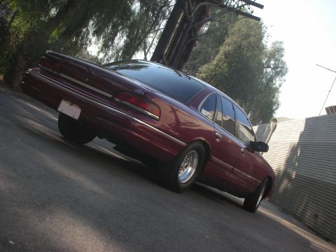 1992 Ford Crown Victoria - A maroon sedan is parked on a street with trees and a building in the background.