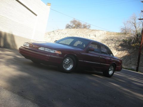 1992 Ford Crown Victoria - A maroon 1992 Ford Crown Victoria is parked on an incline with a building to its left.