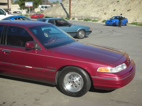 1992 Ford Crown Victoria - A red sedan is parked in a lot with other vehicles, including a blue Ford Mustang.