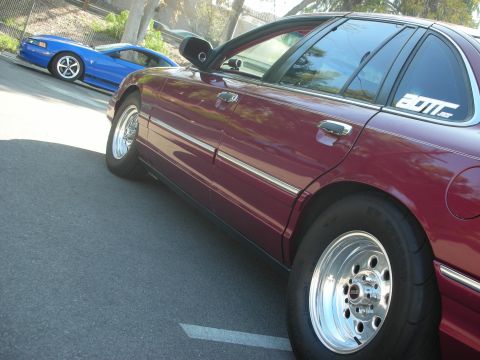 1992 Ford Crown Victoria - Two cars parked on a street, a maroon sedan and a blue sports car.