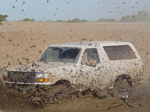 1992 Ford Bronco - Ford Bronco is stuck in the mud, with mud flying everywhere.
