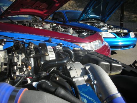 1992 Ford Crown Victoria - Close-up of a supercharged engine bay, with two cars parked side-by-side, hoods open.