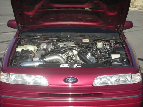 1992 Ford Crown Victoria - Engine bay of a red 1992 Ford Crown Victoria, modified with a turbocharger and intercooler, with the hood open.