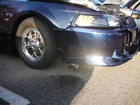 1998 Ford Crown Victoria - A dark blue coupe with custom chrome wheels and an exhaust pipe is parked at an outdoor event.