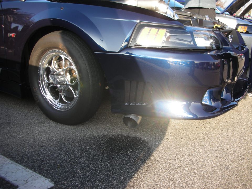 Front corner of dark blue muscle car with polished drag wheel and slick tire