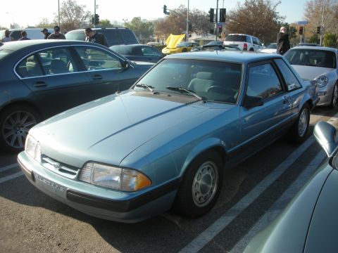 1998 Ford Crown Victoria - A light blue Ford Mustang is parked in a lot with other vehicles around it.
