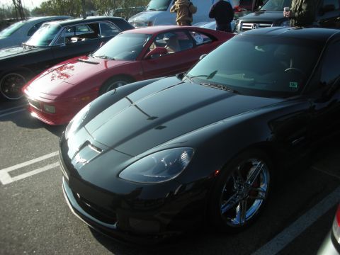 1998 Ford Crown Victoria - A black sports car is parked in a lot next to other vehicles.