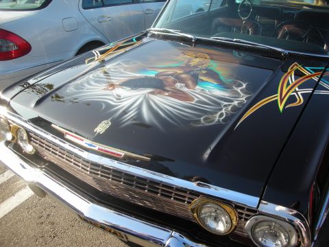 1998 Ford Crown Victoria - A black classic car features detailed airbrushed artwork on its hood, parked next to a modern white sedan.