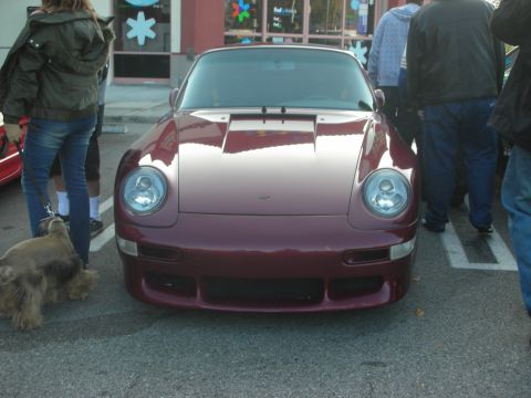1998 Ford Crown Victoria - A maroon Porsche 911 is parked in a lot, with several people and a dog standing around it.