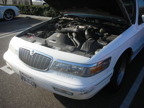 1998 Ford Crown Victoria - A white Mercury Grand Marquis is parked with its hood up, revealing the engine compartment.