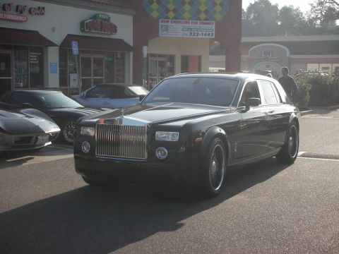 1998 Ford Crown Victoria - A Rolls-Royce Phantom is parked in front of a strip mall with other cars nearby.