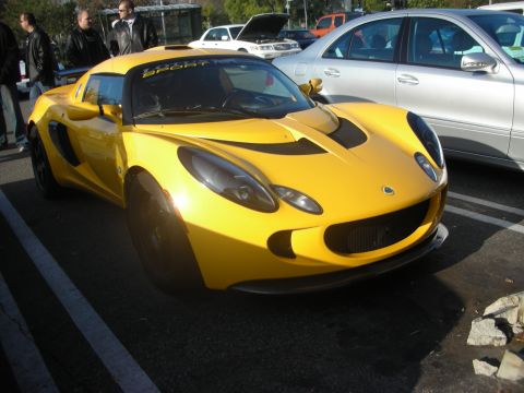 1998 Ford Crown Victoria - A bright yellow Lotus Elise is parked in a lot, with a silver sedan beside it and people standing nearby.