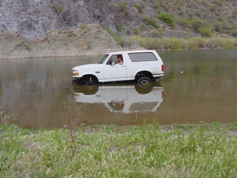 1992 Ford Bronco - A white 1992 Ford Bronco is partially submerged in water, driving towards the shore.