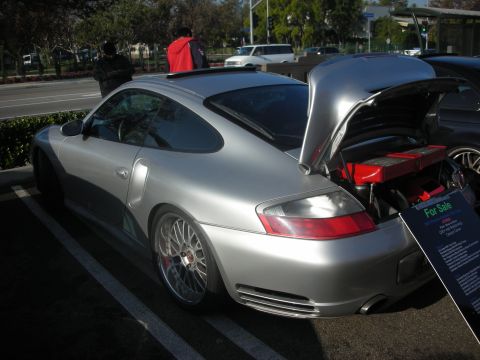 1998 Ford Crown Victoria - A silver Porsche 911 is parked with its rear trunk open, revealing its engine and a 'For Sale' sign.