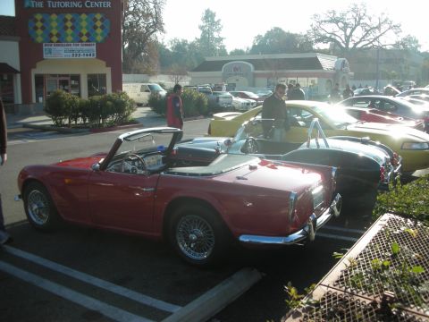 1998 Ford Crown Victoria - A red convertible sports car is parked in a lot with other vehicles, under a bright sky.