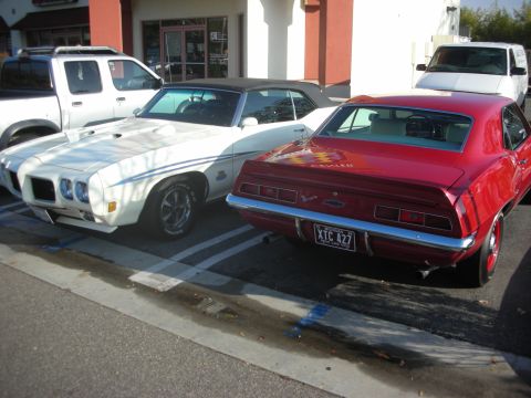 1998 Ford Crown Victoria - Two classic American muscle cars are parked side-by-side in a parking lot.