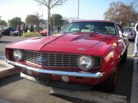 1998 Ford Crown Victoria - A bright red 1969 Chevrolet Camaro is parked at a car meet, its iconic front-end design.