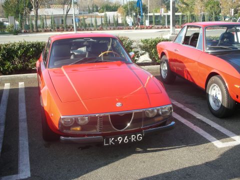 1998 Ford Crown Victoria - Two vintage red sports cars are parked side-by-side in a parking lot on a sunny day.