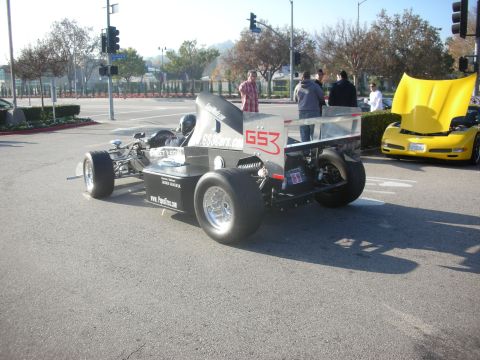 1998 Ford Crown Victoria - Two cars are parked on a street, one a race car and the other a yellow sports car with its hood open.