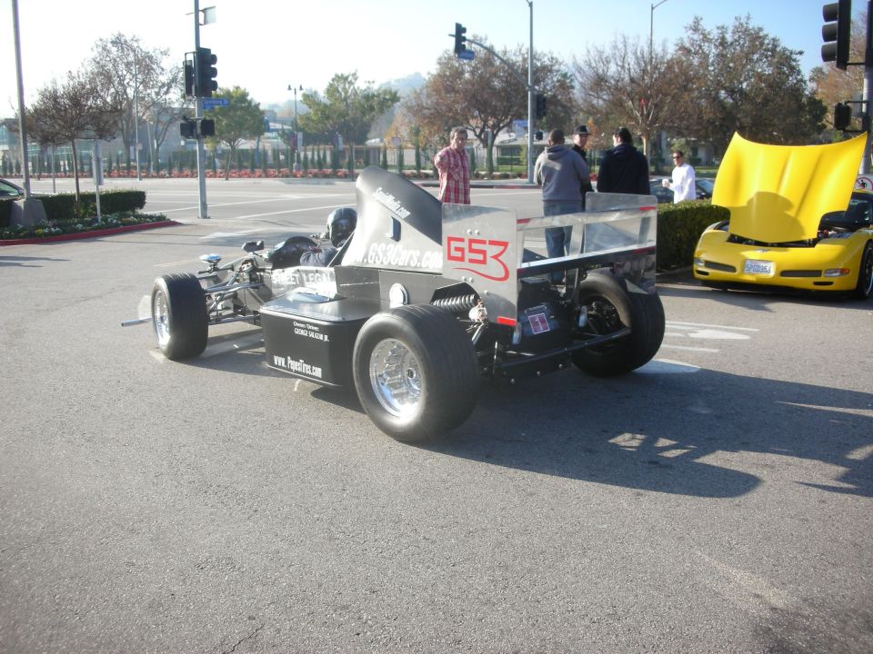 Silver open-wheel formula-style race car parked at a street intersection